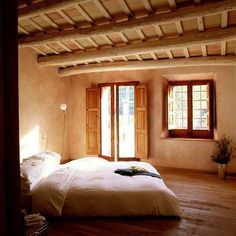 a bed sitting in the middle of a room next to two windows and a wooden floor