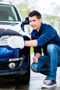 a man is washing his car with a sponge on the front windshield and smiling at the camera