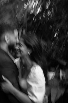 black and white photograph of two people hugging each other in front of trees with blurry background