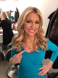 a woman standing in front of a mirror wearing a blue shirt and gold jewelry necklace