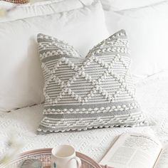 a coffee cup on a tray next to a pillow and an open book sitting on a bed