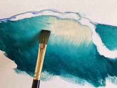 a paintbrush sitting on top of a piece of paper next to an ocean painting