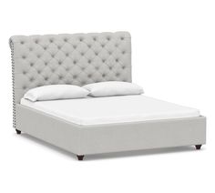 an upholstered bed frame with white pillows and buttons on the headboard is shown