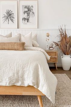 a bed with white linens and pillows in a bedroom next to two pictures on the wall