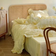 a bed with yellow sheets and pillows in a room next to a wooden table on which is a wicker chair