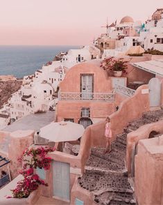 a woman is walking up the stairs to an old village by the ocean with umbrellas