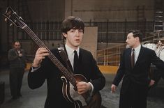 two men in suits and ties are playing guitars while one man is holding an instrument