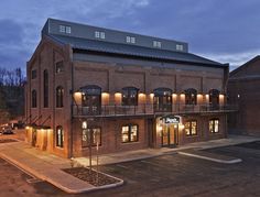 an empty parking lot in front of a large brick building with lights on the windows