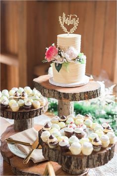 three tiered cake and cupcakes are displayed on wood slices at the reception table