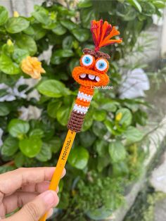 a hand holding a crocheted pencil with an orange and white face on it