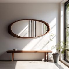 a round mirror hanging on the wall above a wooden bench in front of a window