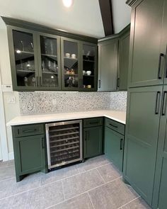 an empty kitchen with green cabinets and white counter tops, including a wine cooler in the center