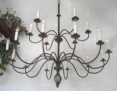 a chandelier with many lit candles hanging from it's sides and some potted plants in the background