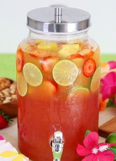 a jar filled with fruit and lemonade on top of a table next to flowers