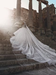 a woman in a wedding dress is standing on some steps with her veil flowing over her head