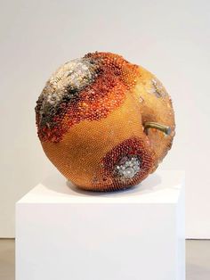 an orange sculpture sitting on top of a white pedestal in front of a white wall