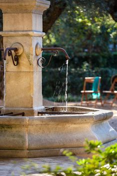 an outdoor fountain with water running from it's spout and some chairs in the background