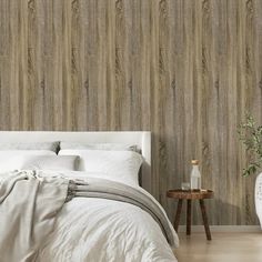 a white bed sitting next to a wooden wallpaper covered in wood planks on top of a hard wood floor