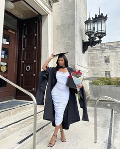 a woman in a graduation gown is standing on the steps with flowers and a coat over her head