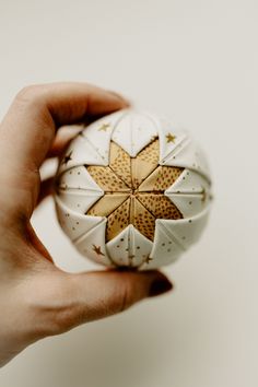 a hand holding a white and gold ornament