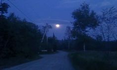 the full moon is seen over a road in the distance with trees on both sides