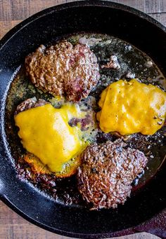 some meat patties are cooking in a skillet on the stove top with yellow sauce