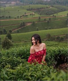 a woman sitting in the middle of a lush green field with hills and trees behind her