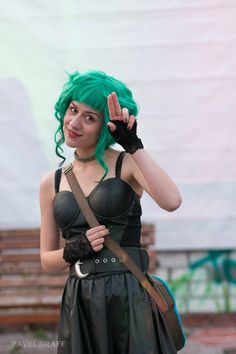 a woman with green hair wearing a black dress and holding her hand up in the air