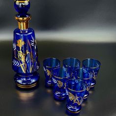 a set of blue glass cups and a vase with gold designs on it sitting next to each other