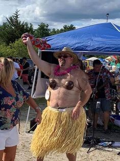 a man in a hula skirt standing on the beach with his hands up and other people around him