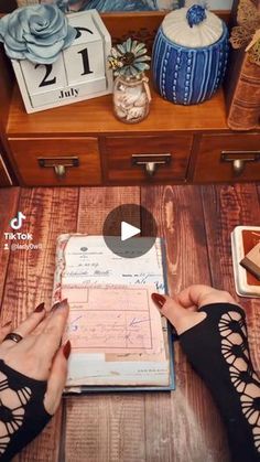 a person is writing on a book in front of a wooden table with other items