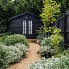 a small black cabin surrounded by trees and bushes with a path leading up to it