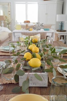 the table is set with lemons and greenery in glass vases on each side