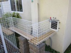 a white wire cage is attached to the side of a house with two brick pillars