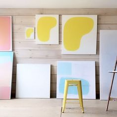 a room with paintings on the wall and a yellow stool in front of one chair