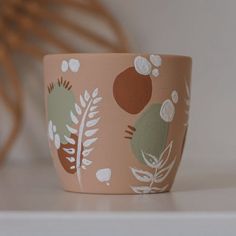 a close up of a cup on a shelf with plants and leaves painted on it