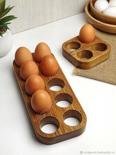 an egg tray with six eggs in it on a white table next to two bowls and a pine plant