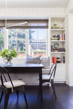 a dining room table with two chairs and a bench in front of a window filled with books