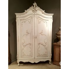 an antique white armoire with ornate carvings on the top and bottom panel, in a bedroom