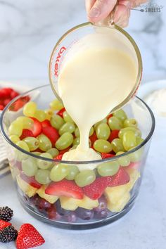 someone pouring milk into a glass bowl filled with mixed fruits and berries for a fruit salad