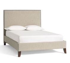 an upholstered bed with white pillows and linens on the headboard is shown