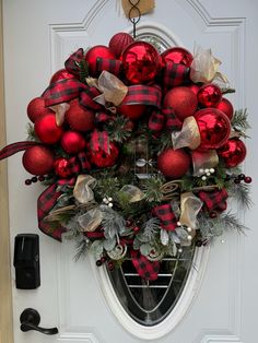 a red and black christmas wreath on the front door with ornaments hanging from it's side