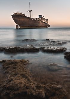 an old rusty ship sitting on top of the ocean next to rocks and water at sunset