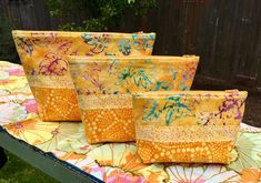 four bags sitting on top of a table covered in yellow and pink fabric with flowers