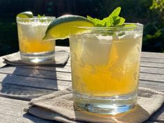 two glasses filled with lemonade and lime on top of a wooden picnic table outdoors