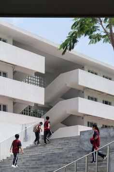 some people are walking up and down the stairs in front of an apartment building with white balconies