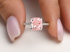 a woman's hand holding an engagement ring with a pink diamond in the center