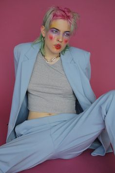 a woman with pink hair and makeup sitting on the ground