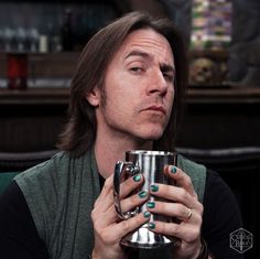 a man with long hair holding a metal cup in his hands and looking at the camera