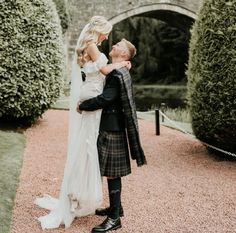 a bride and groom standing in front of a stone bridge at their scottish wedding ceremony